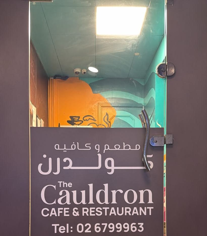 The Cauldron Café & Restaurant entrance sign on Mina Road, in Arabic and English, with the landline 02 679 9963
